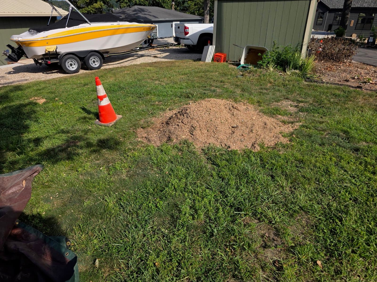 Pile of fresh grindings beside the lakeside shed after the stump was removed, boat in the background