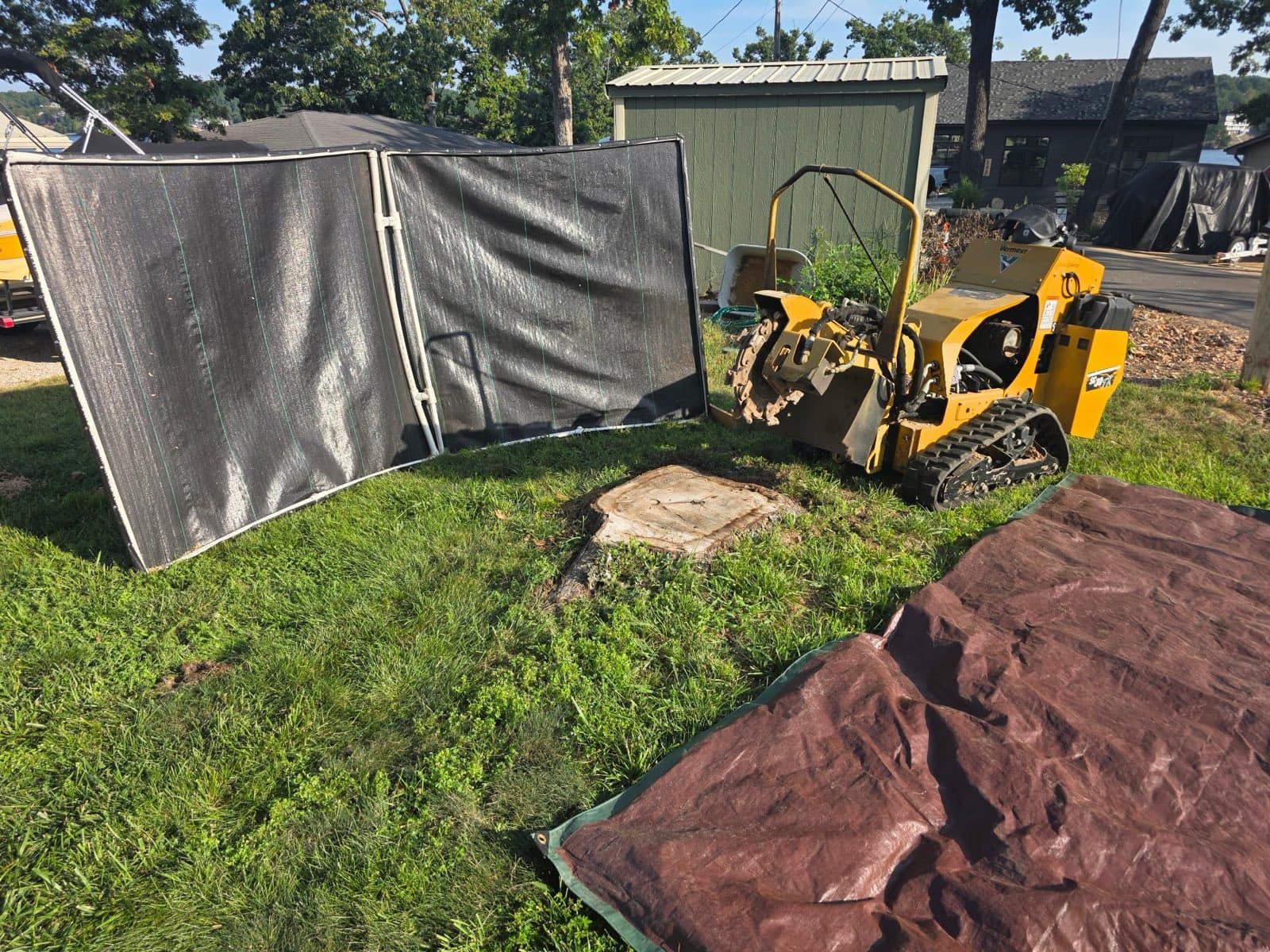 Grinder set up behind debris screens and a tarp around a stump next to a lakeside shed