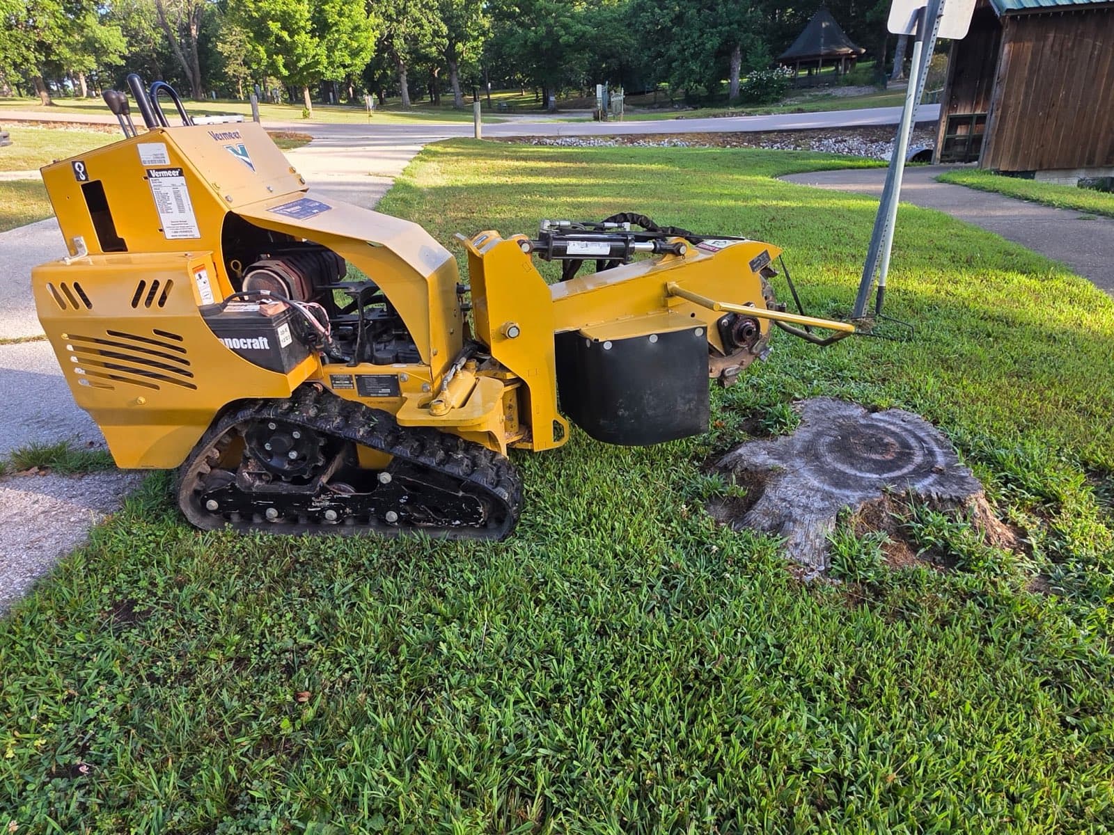 Vermeer tracked stump grinder parked beside a cut stump on a green lawn